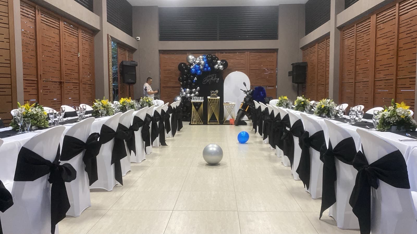 Salón de evento con mesas vestidas y arco de globos, montaje de Aura Sabor en Ibagué